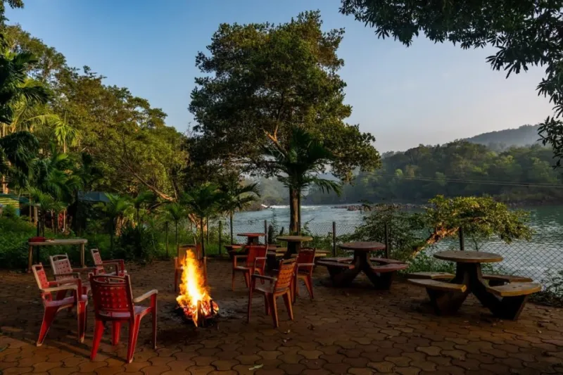 Campfire and seating on a paved riverside terrace beside the Kali river at dusk