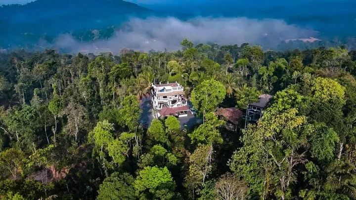 Aerial view of the property among dense forest, with mist over the Coorg hills