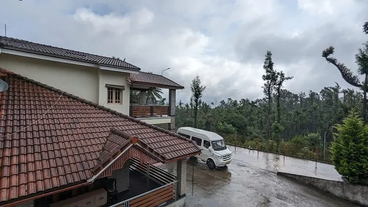 Tiled-roof homestay and driveway with a tempo traveller, surrounded by hills and trees near Mudigere
