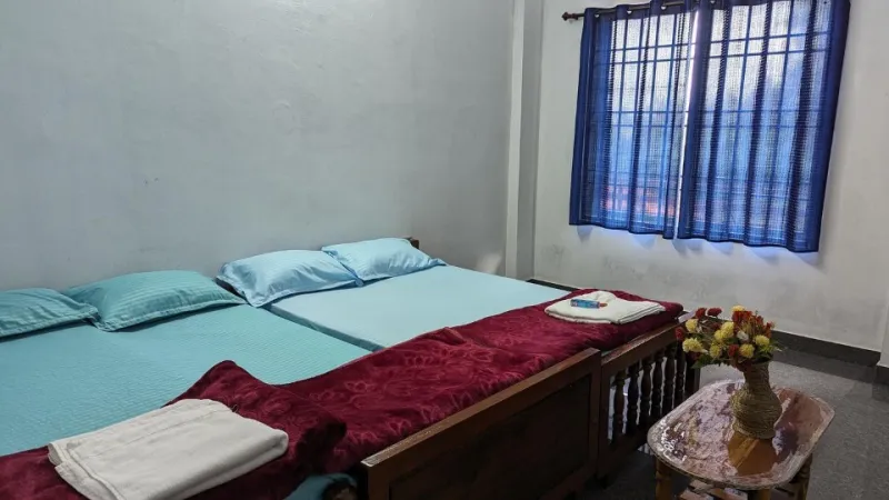 Room with two beds in light blue linen, maroon blankets and a flower vase