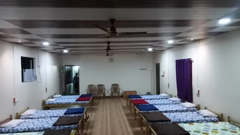 Large dormitory hall with rows of single beds and ceiling fans
