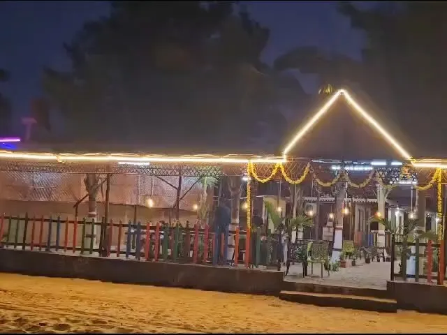 Entrance lit with string lights and marigold garlands at night, with a colourful fence on the sand