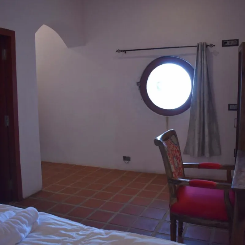 Room with a round porthole window and a carved red chair